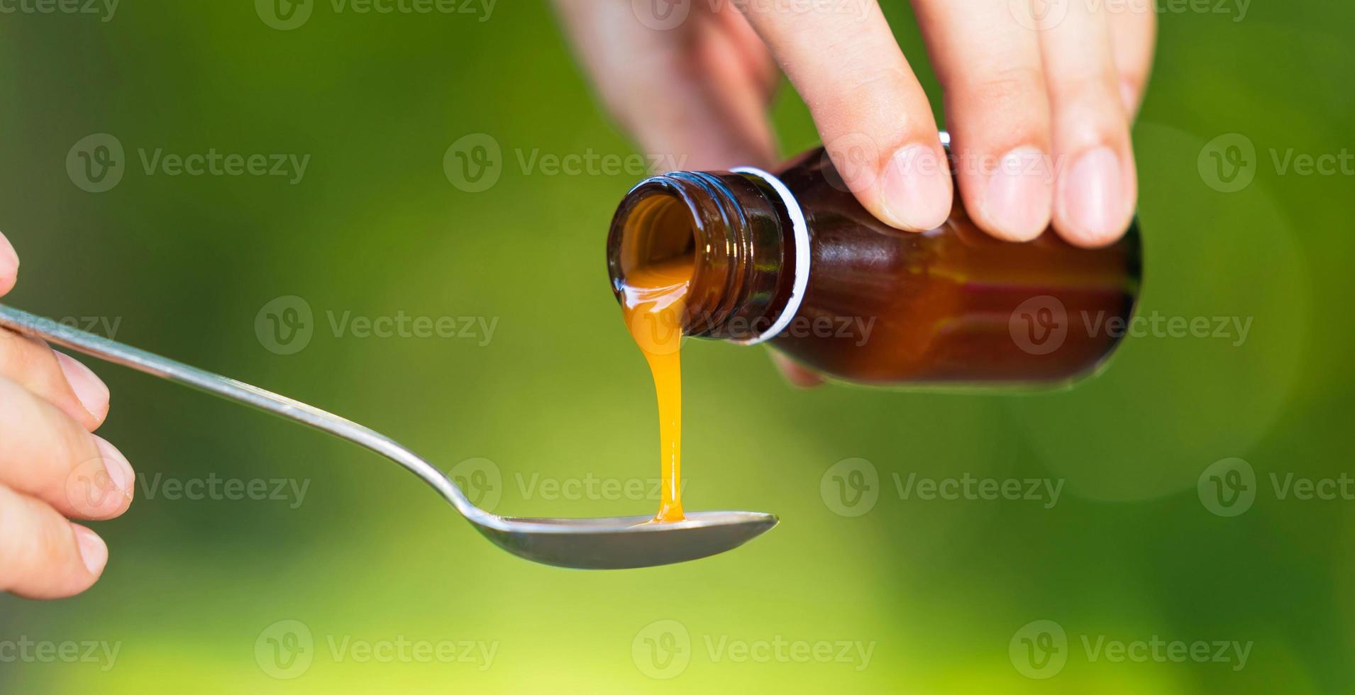 Man hand pouring medication or antipyretic syrup from bottle to spoon photo