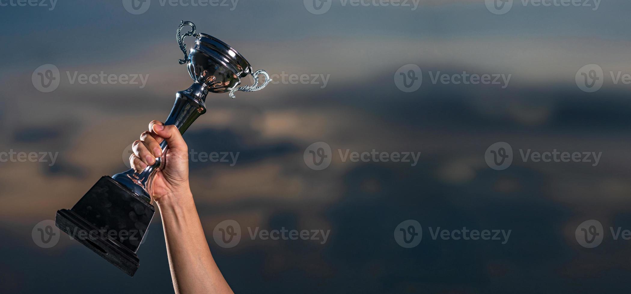 A man holding up a trophy cup on against cloudy twilight sky background photo