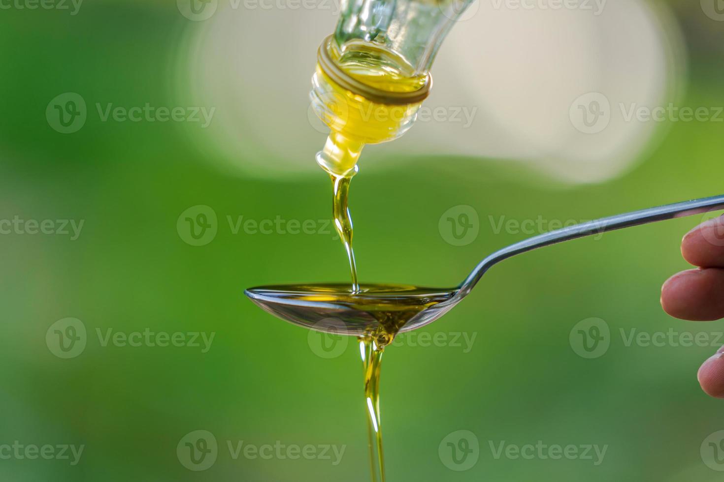 Pouring olive oil into spoon on green park garden background photo