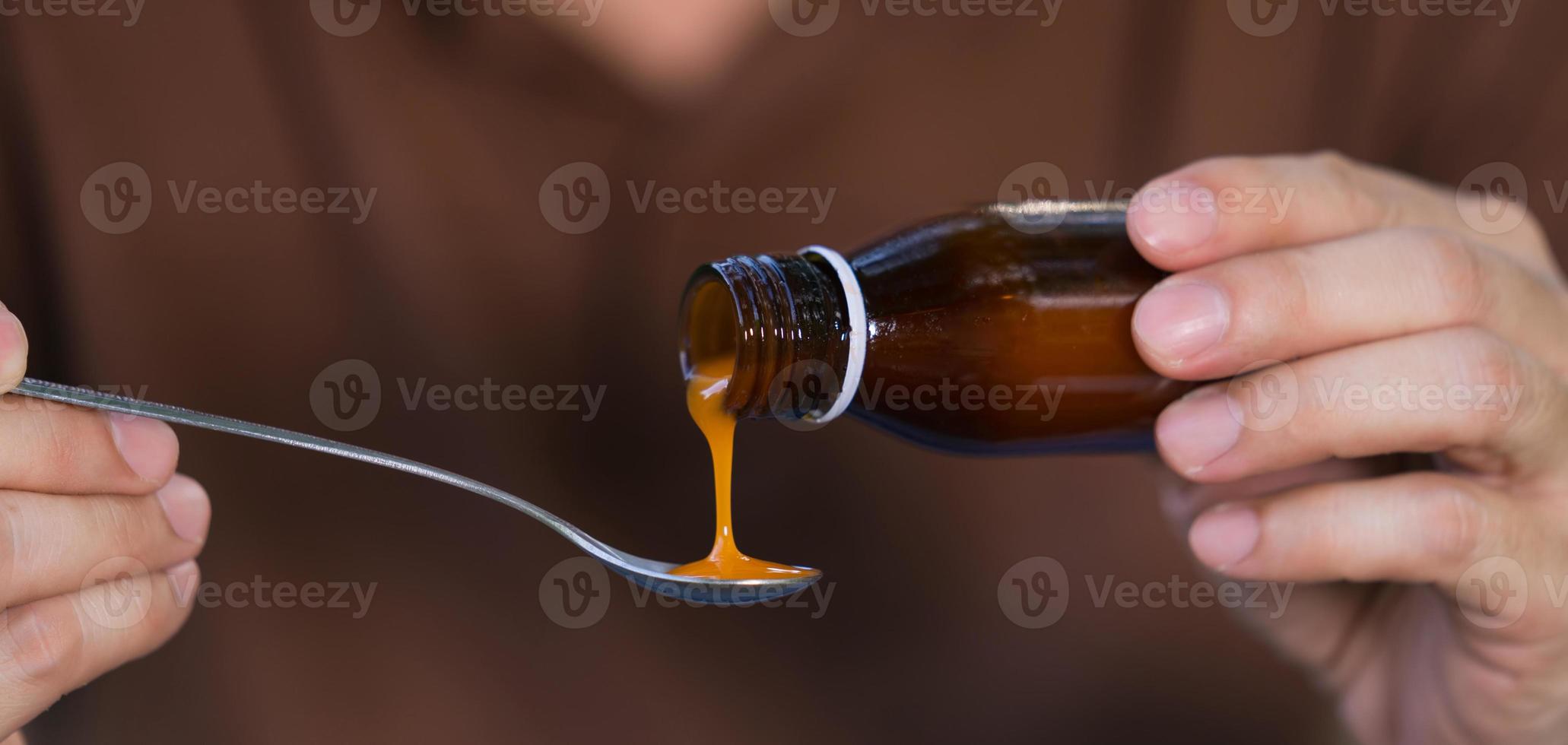 Mano de hombre vertiendo medicación o jarabe antipirético de botella a cuchara foto