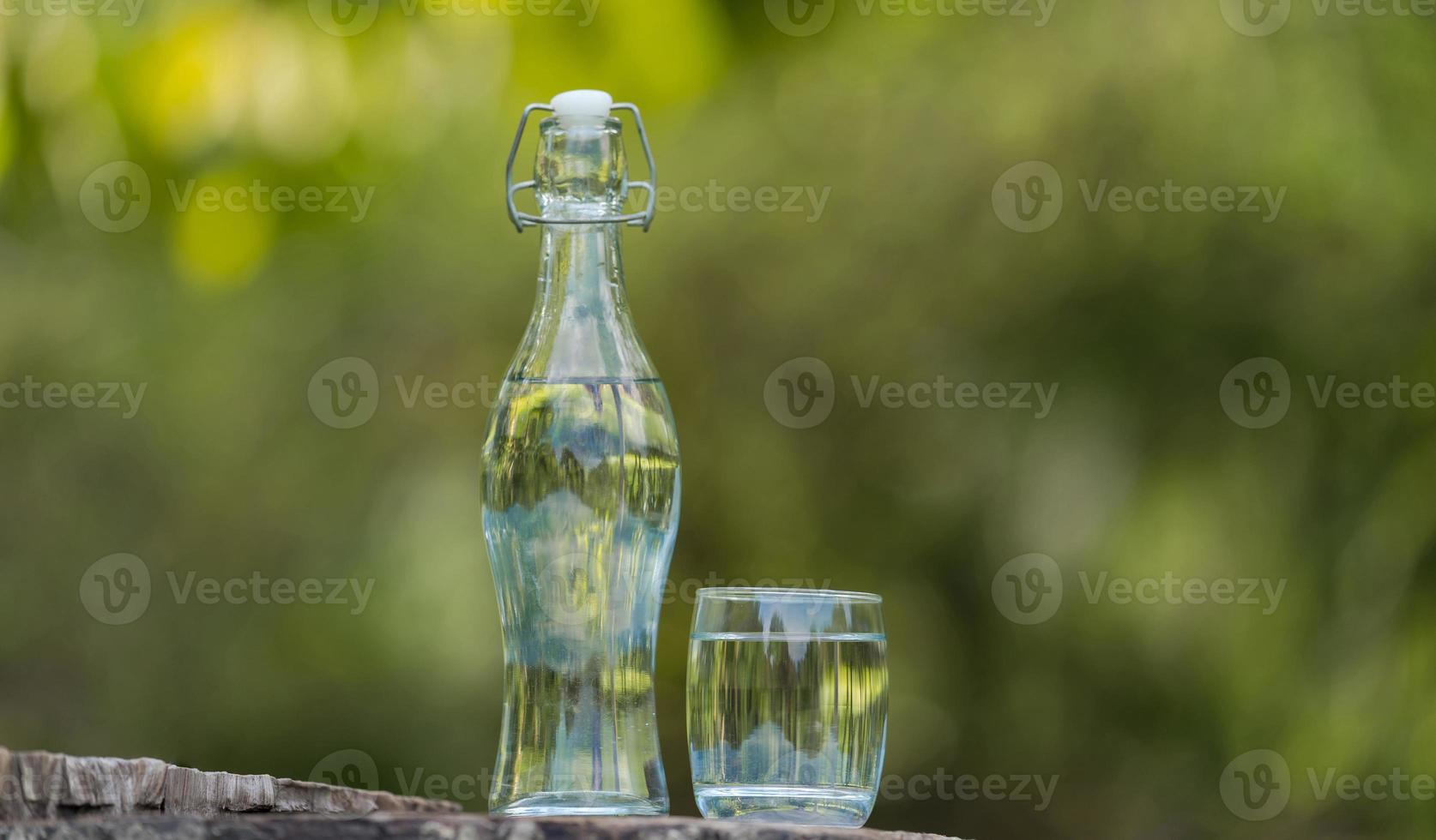 Botella de agua potable y vaso con fondo natural. foto