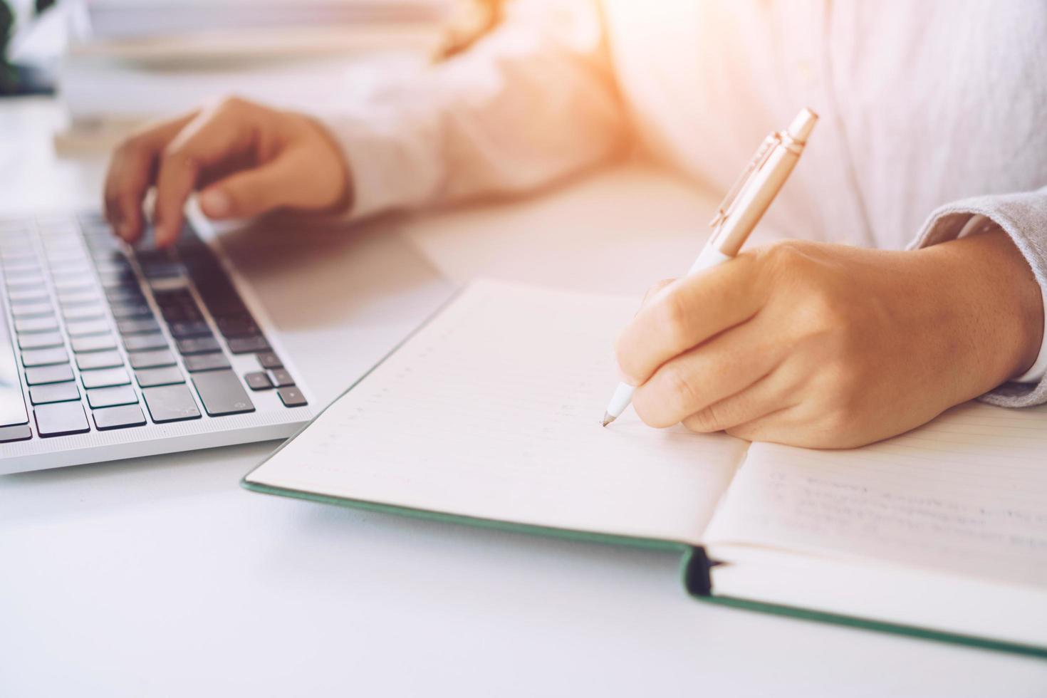 Woman writing in a planner notebook while using laptop at home photo