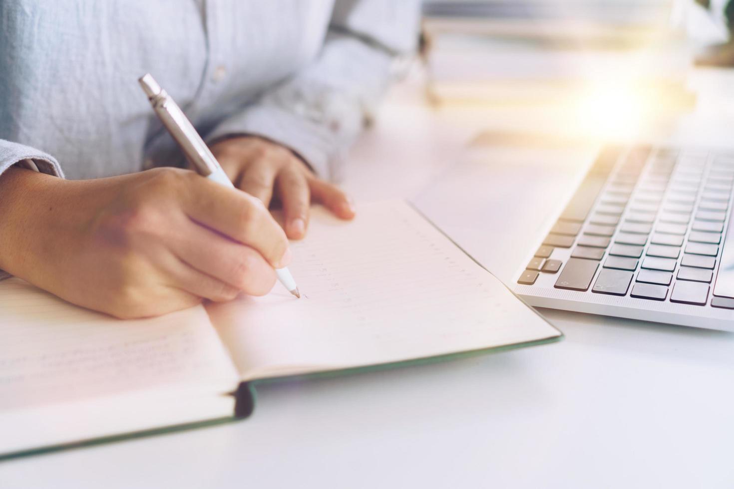 Woman writing in a planner notebook while using laptop at home photo