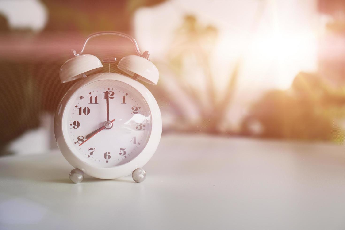 Selective focus of alarm clock showing 8 o'clock on table with nature bokeh background photo