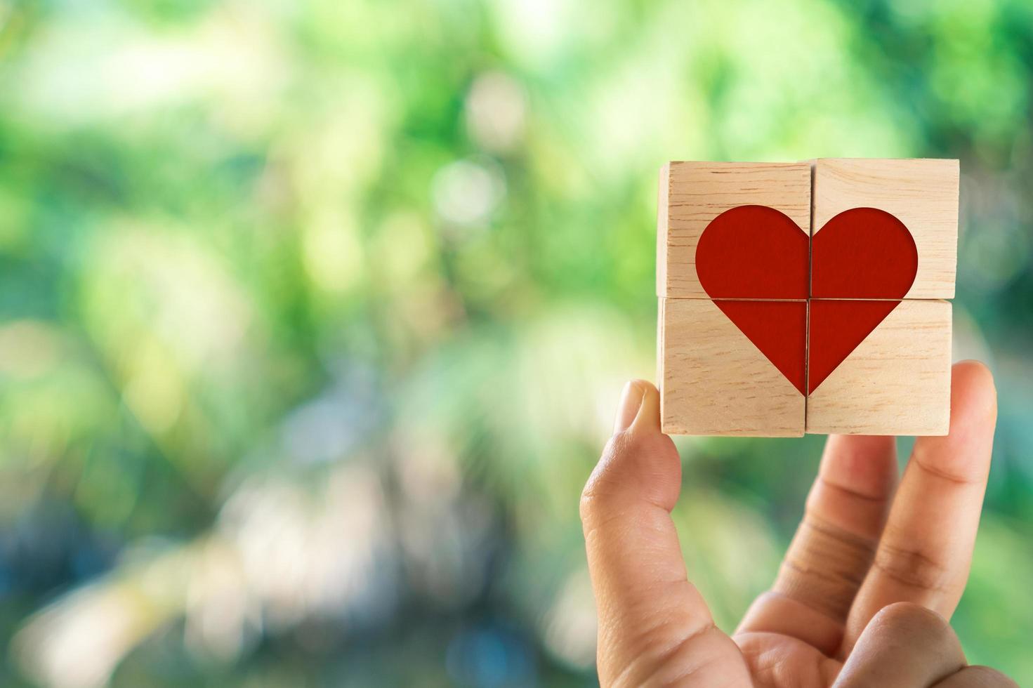 Mano sosteniendo un cubo de madera con icono de signo de corazón con luz solar natural foto