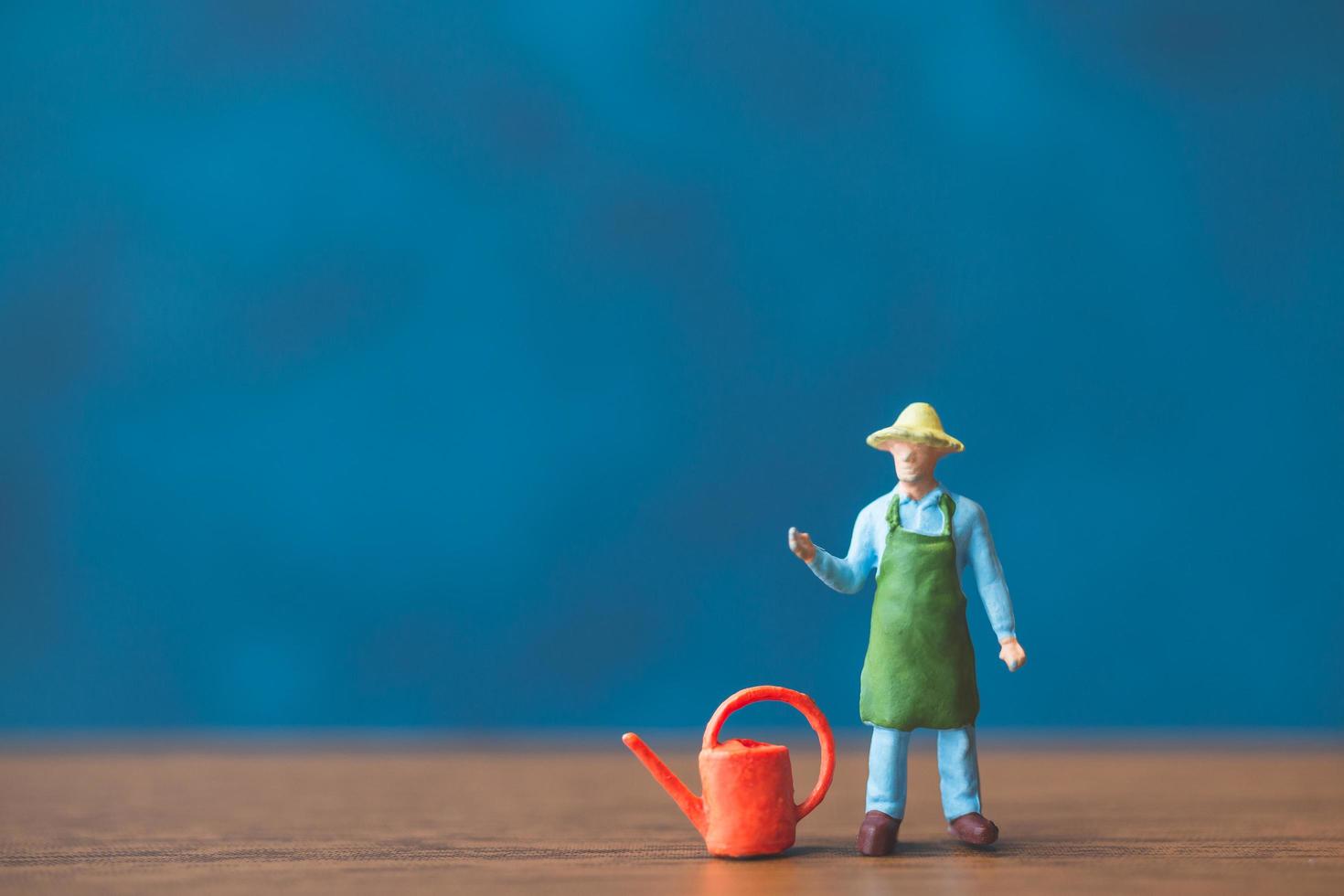 Jardinero en miniatura de pie delante de una pared azul de fondo foto
