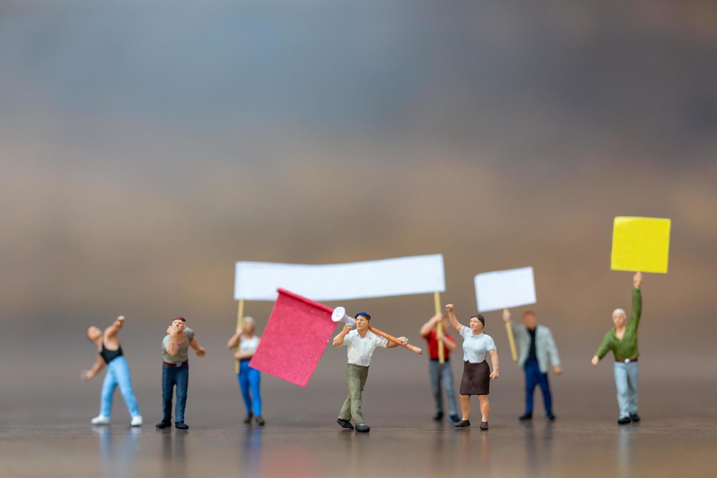 Multitud de manifestantes en miniatura levantando sus manos y gritando sobre un fondo de madera foto