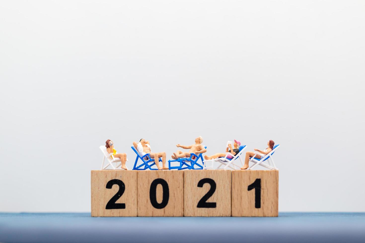 Miniature people wearing swimsuits sitting on wooden blocks with numbers 2021 photo