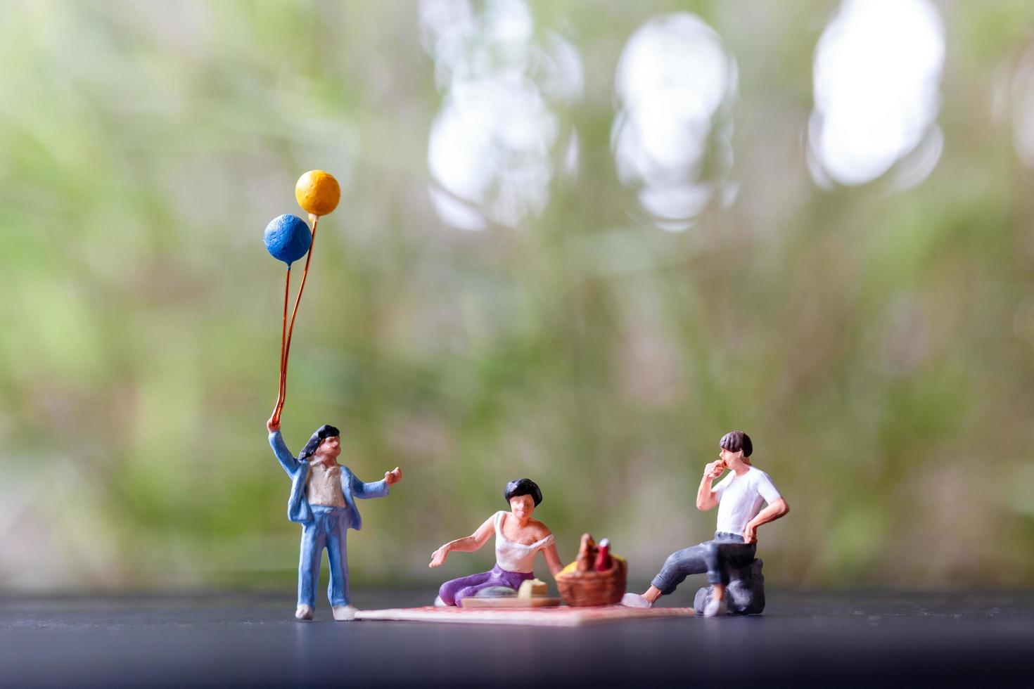 Gente en miniatura de una familia feliz sentada en una estera durante un picnic en el parque foto