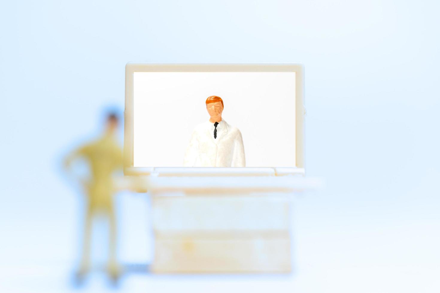 Gente en miniatura de un paciente masculino que consulta con un médico mediante videollamada en una computadora portátil, concepto médico en línea foto