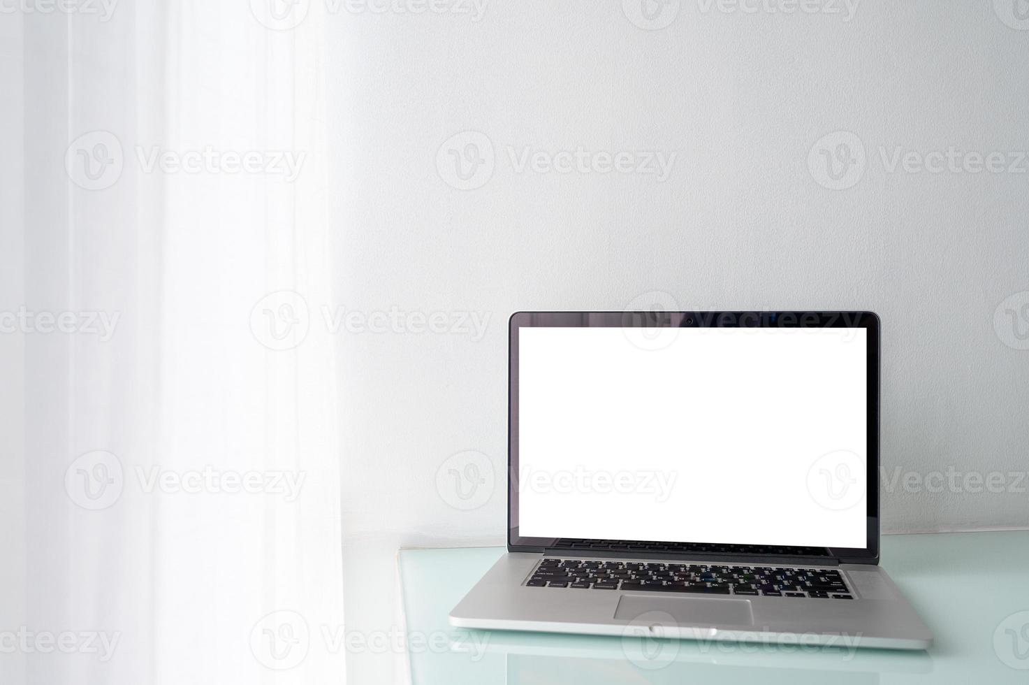 Pantalla en blanco de la computadora portátil en la mesa con pared blanca y cortina blanca foto