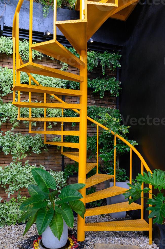 Yellow spiral staircase with plants on brick wall photo