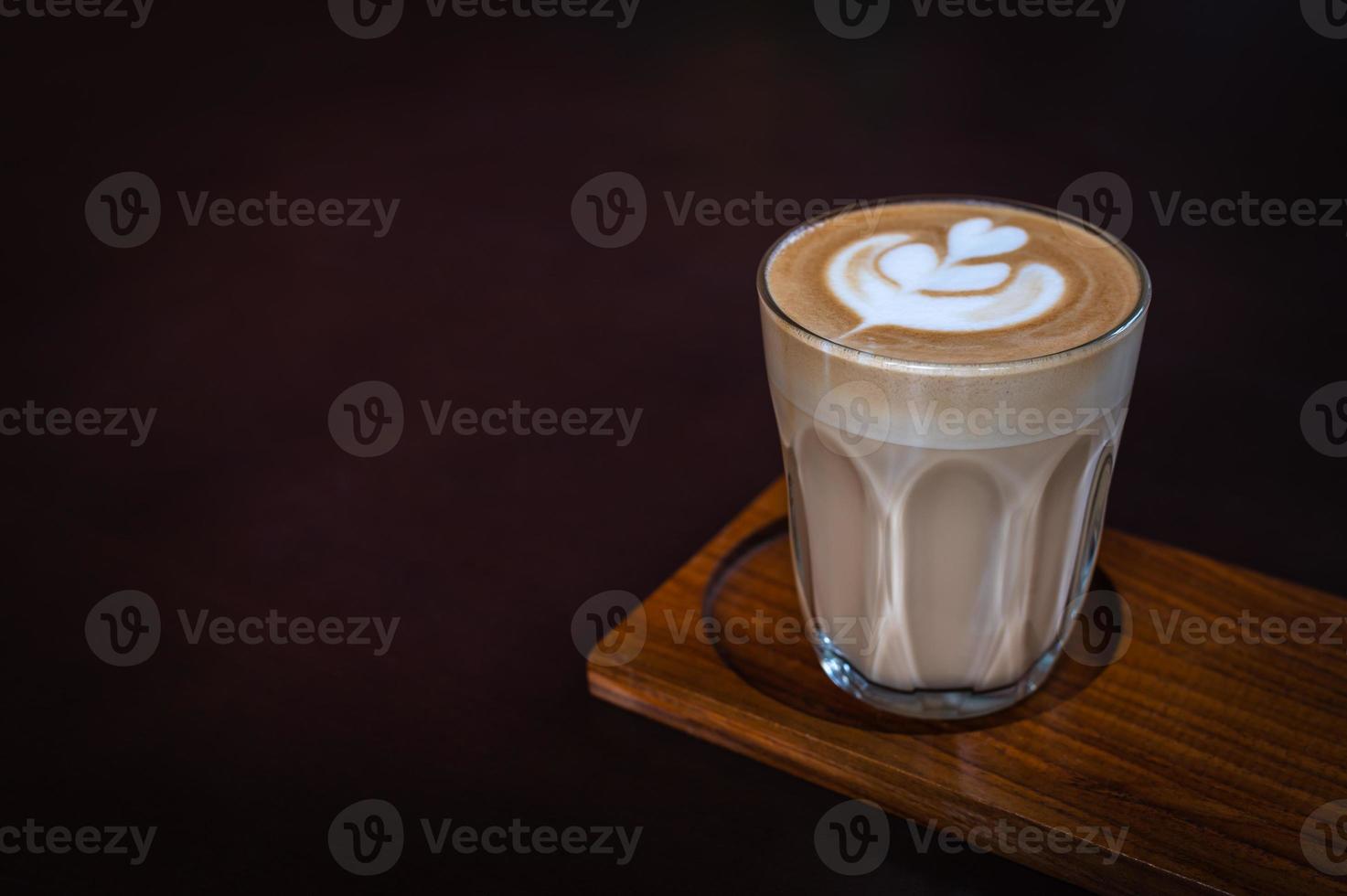 un vaso de latte art en una placa de madera con fondo oscuro foto