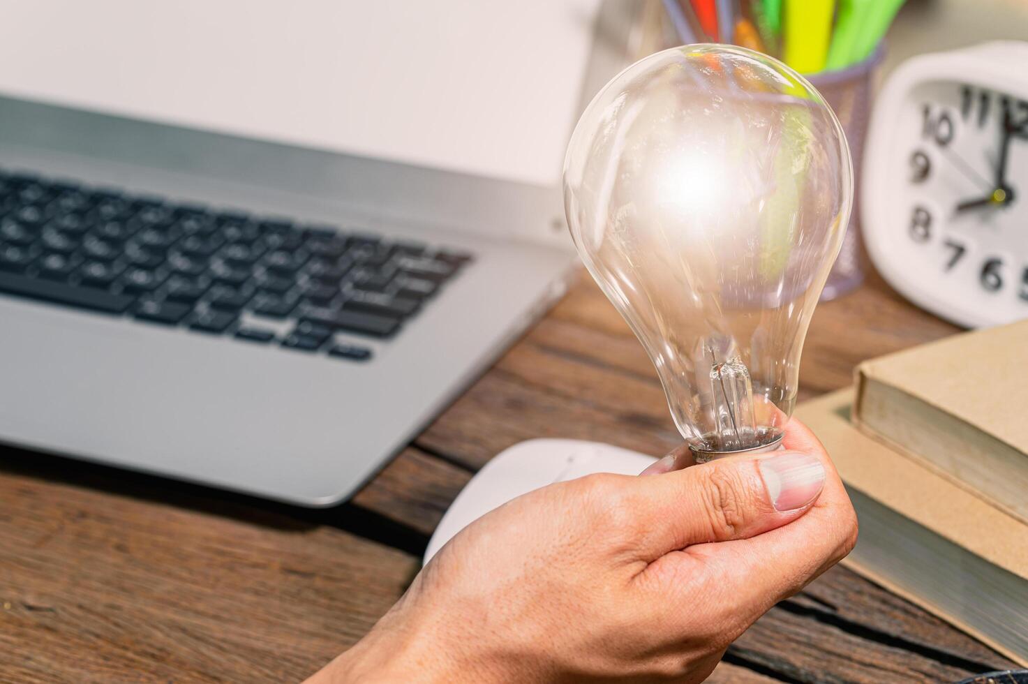 A man holding a light bulb gear symbol while using a computer photo