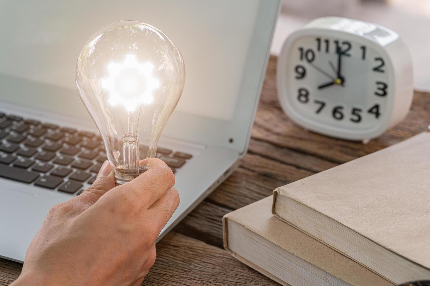 A man holding a light bulb gear symbol while using a computer photo