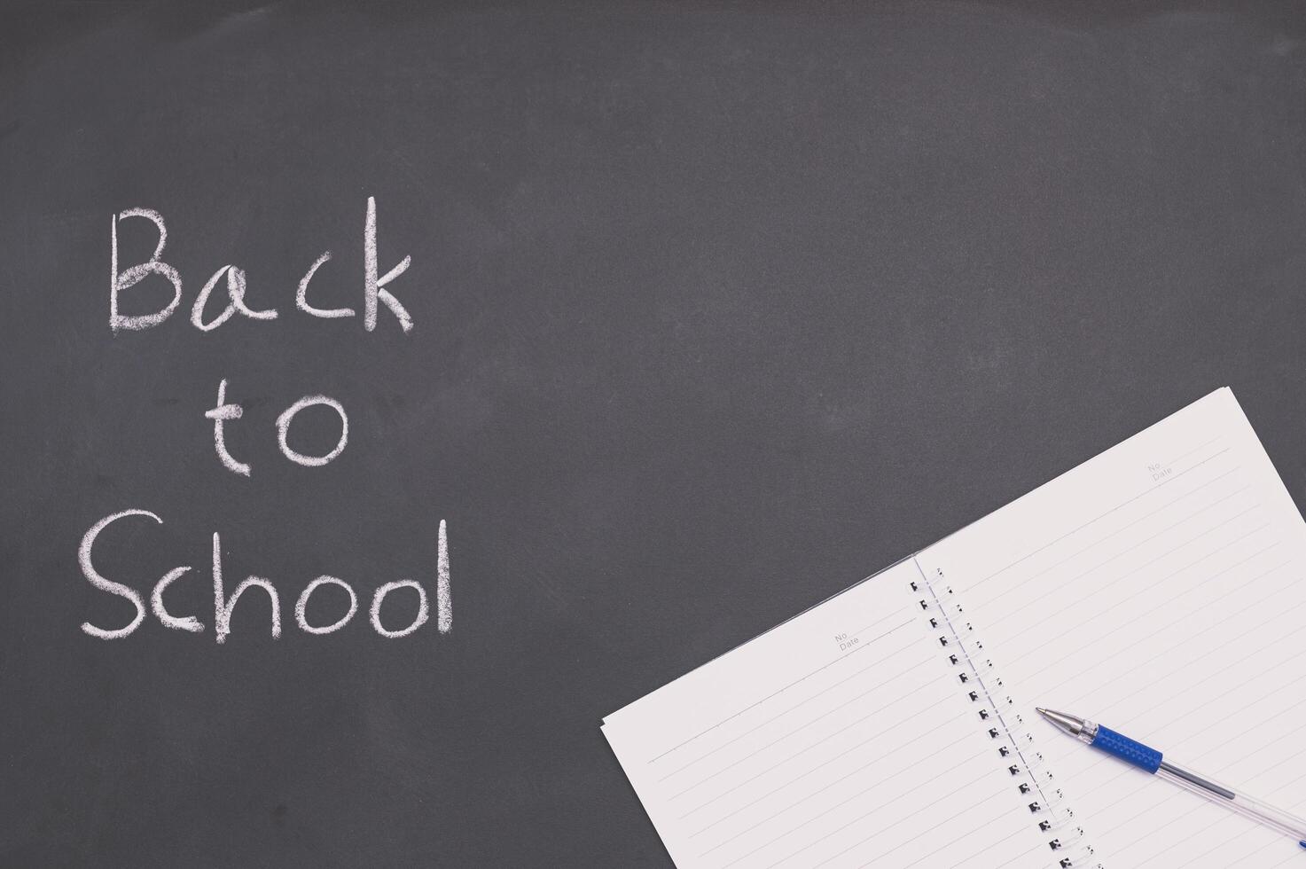 A white notebook with a pen on a chalkboard, back to school and education concept photo