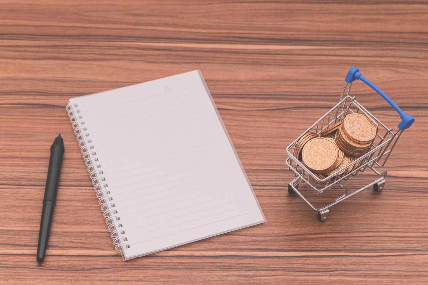 Cuaderno en el escritorio con monedas en un carrito diminuto foto