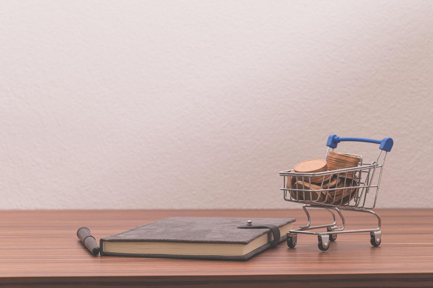 Notebook on the desk with coins in a tiny cart photo