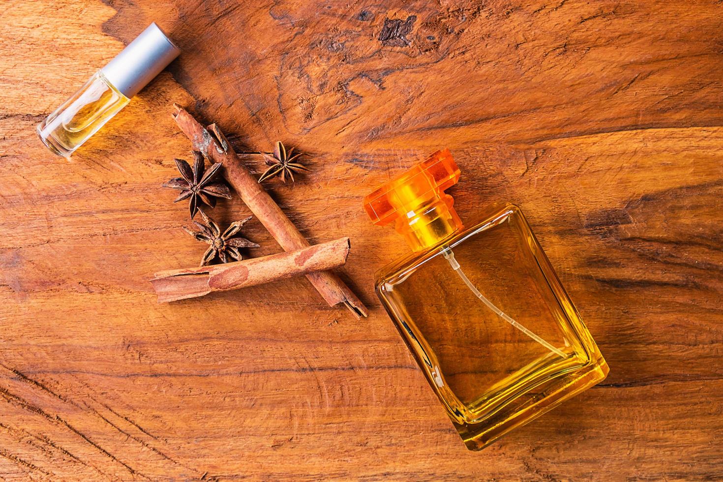 Bottles of perfume, cinnamon sticks, and anise seeds on a wood table photo