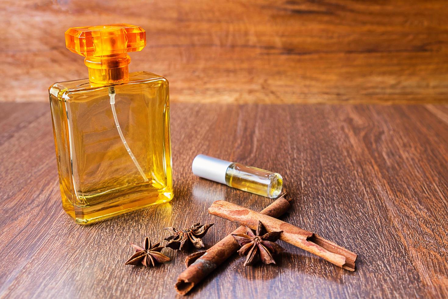 Bottles of perfume, cinnamon sticks, and anise seeds on a wood table photo