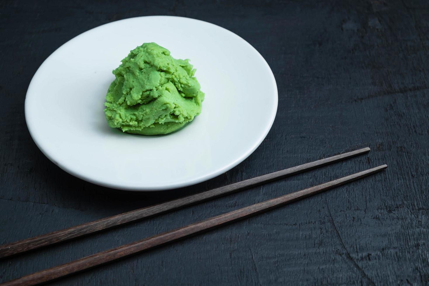 Wasabi on white plate with pair of chopsticks on black table background photo