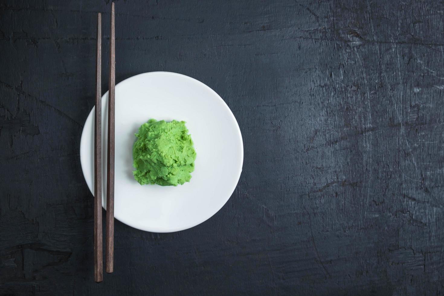 Wasabi on white plate with pair of chopsticks on black table background photo