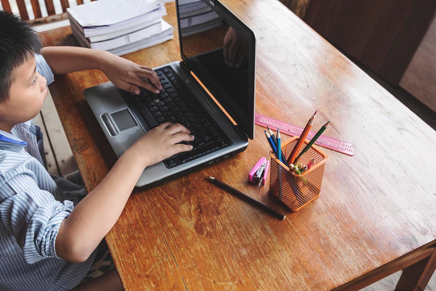 Boy working on a laptop next to cup of pencils on a wooden desk photo