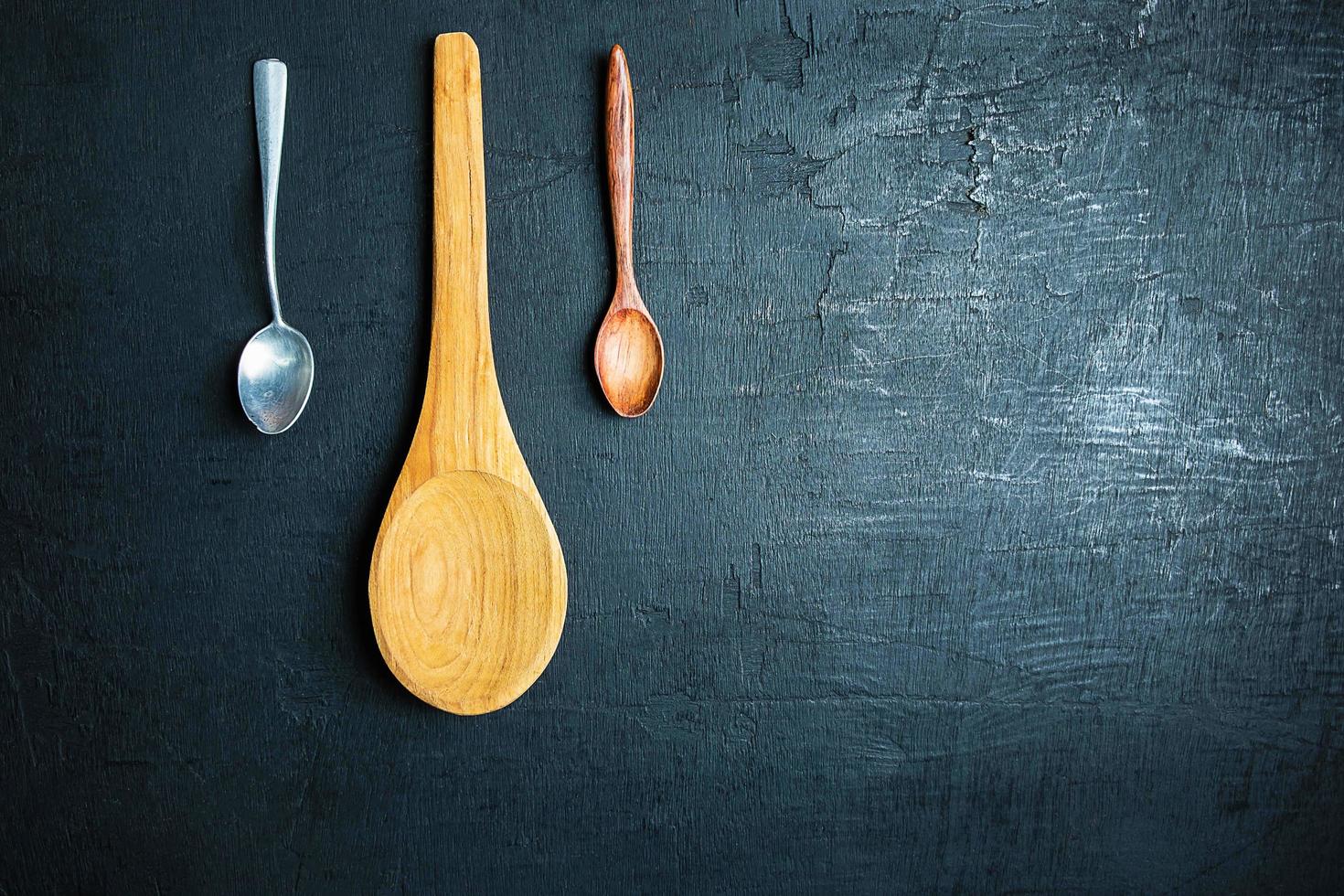 Two wooden spoons and a metal spoon on a black table background photo