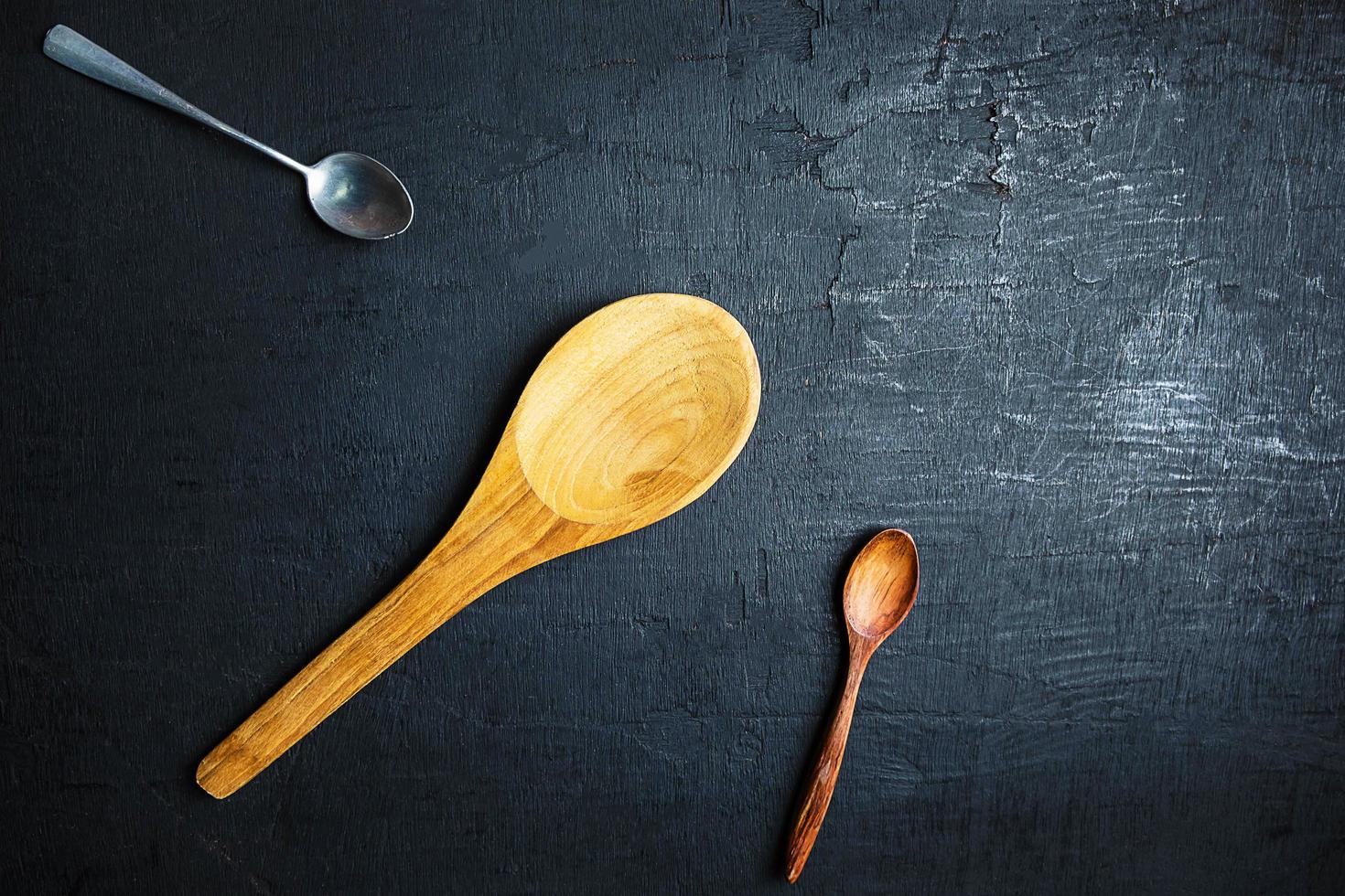 Dos cucharas de madera y una cuchara de metal sobre un fondo de tabla negro foto