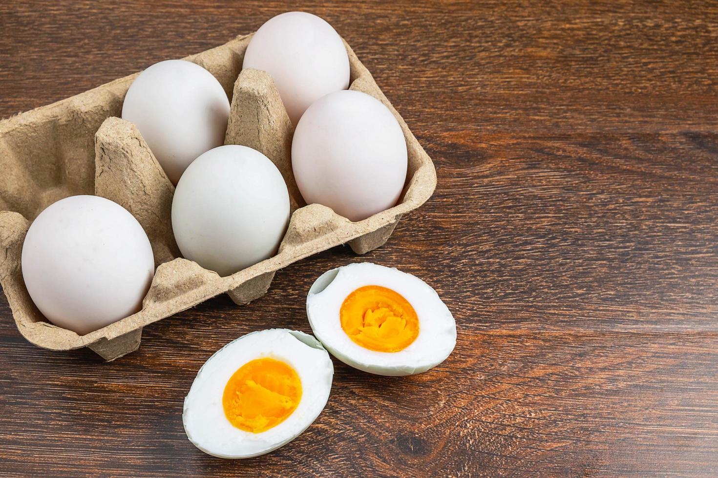 Sliced hard-boiled duck egg next to whole eggs in a carton on a wooden