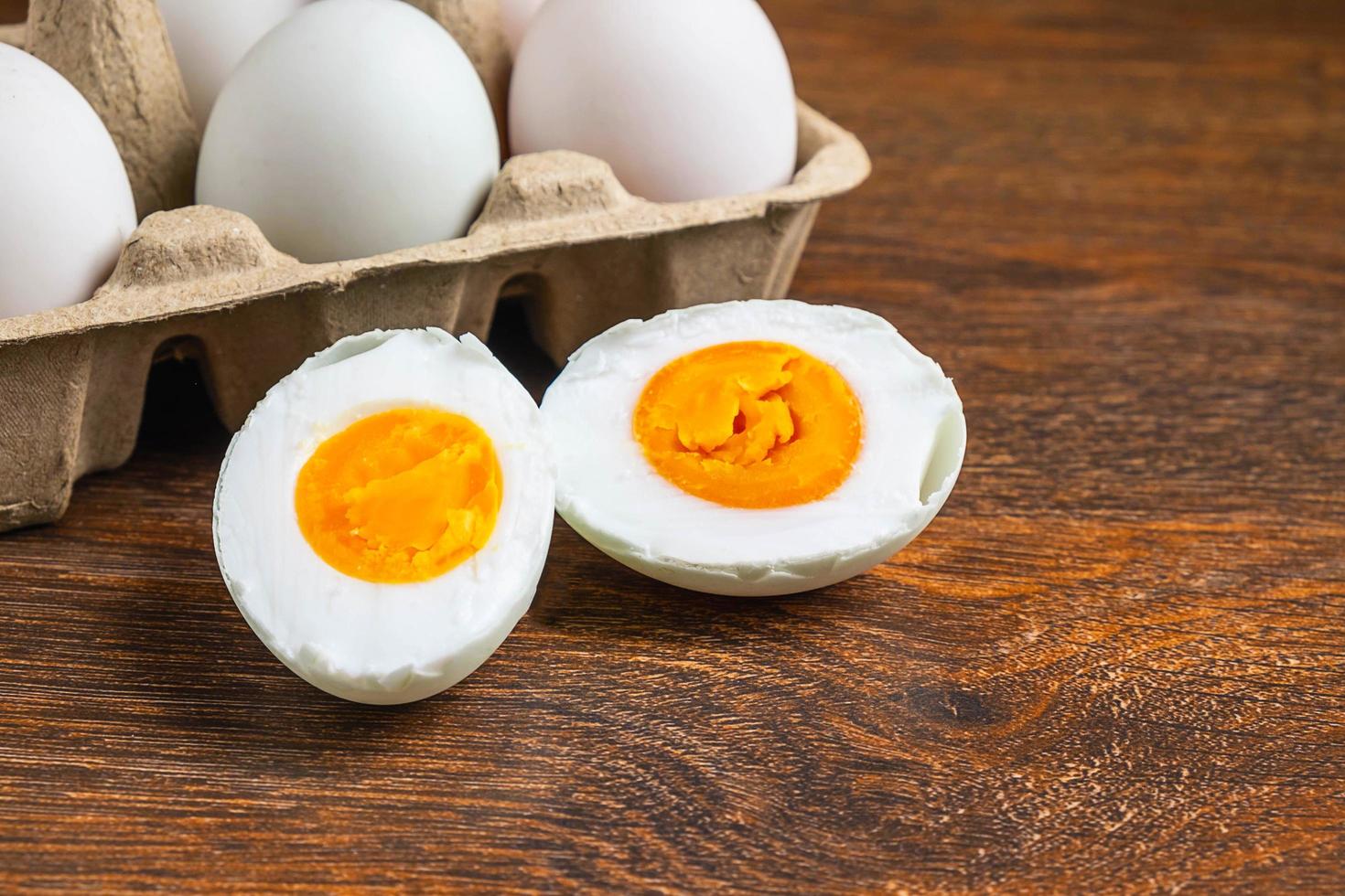 Sliced hard-boiled duck egg next to whole eggs in a carton on a wooden table photo