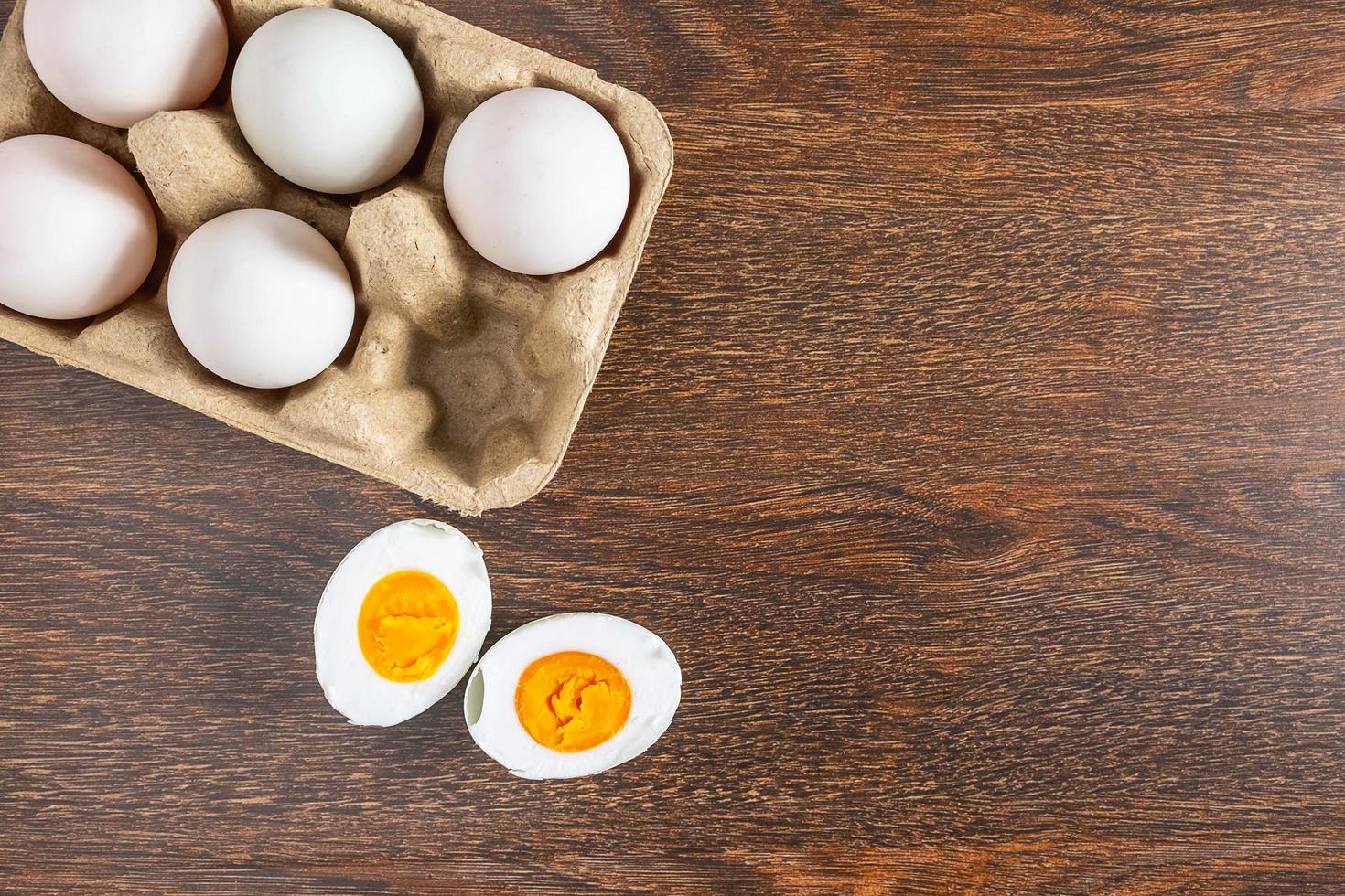 Huevo de pato cocido a la mitad junto a huevos enteros en una caja de cartón sobre una mesa de madera foto