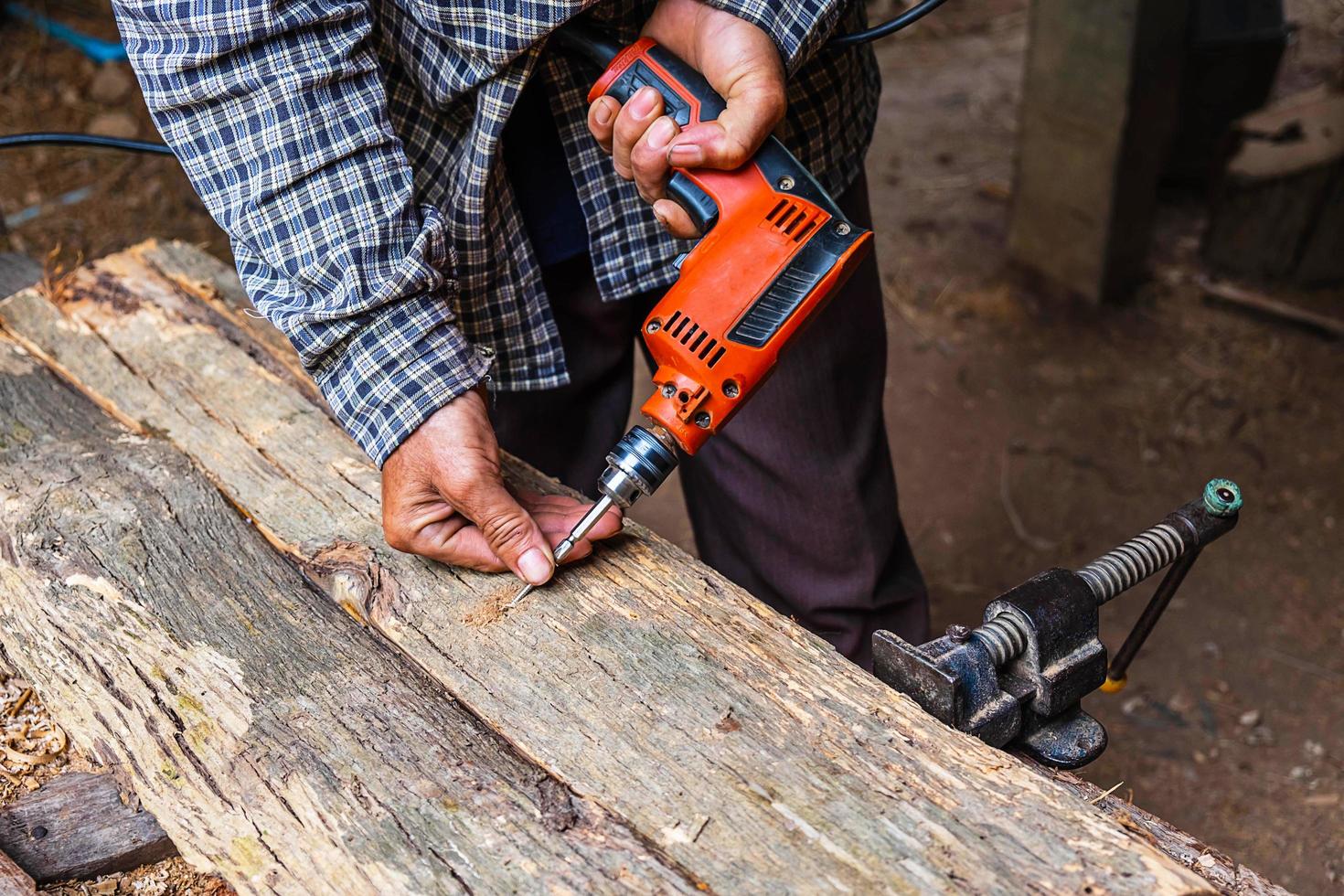 Hombre con taladro eléctrico en la plancha de madera en un taller de carpintería foto