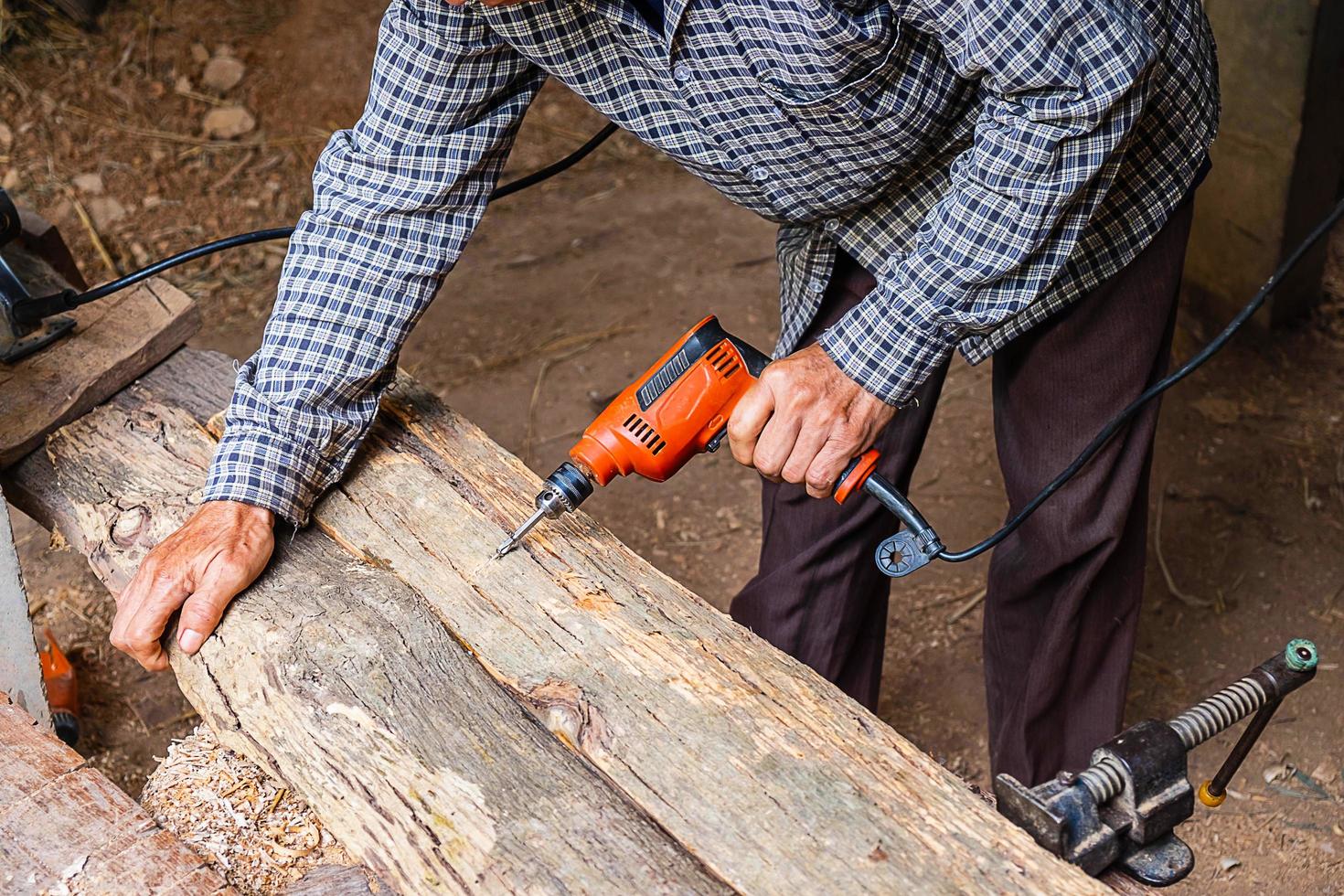 Hombre con taladro eléctrico en la plancha de madera en un taller de carpintería foto