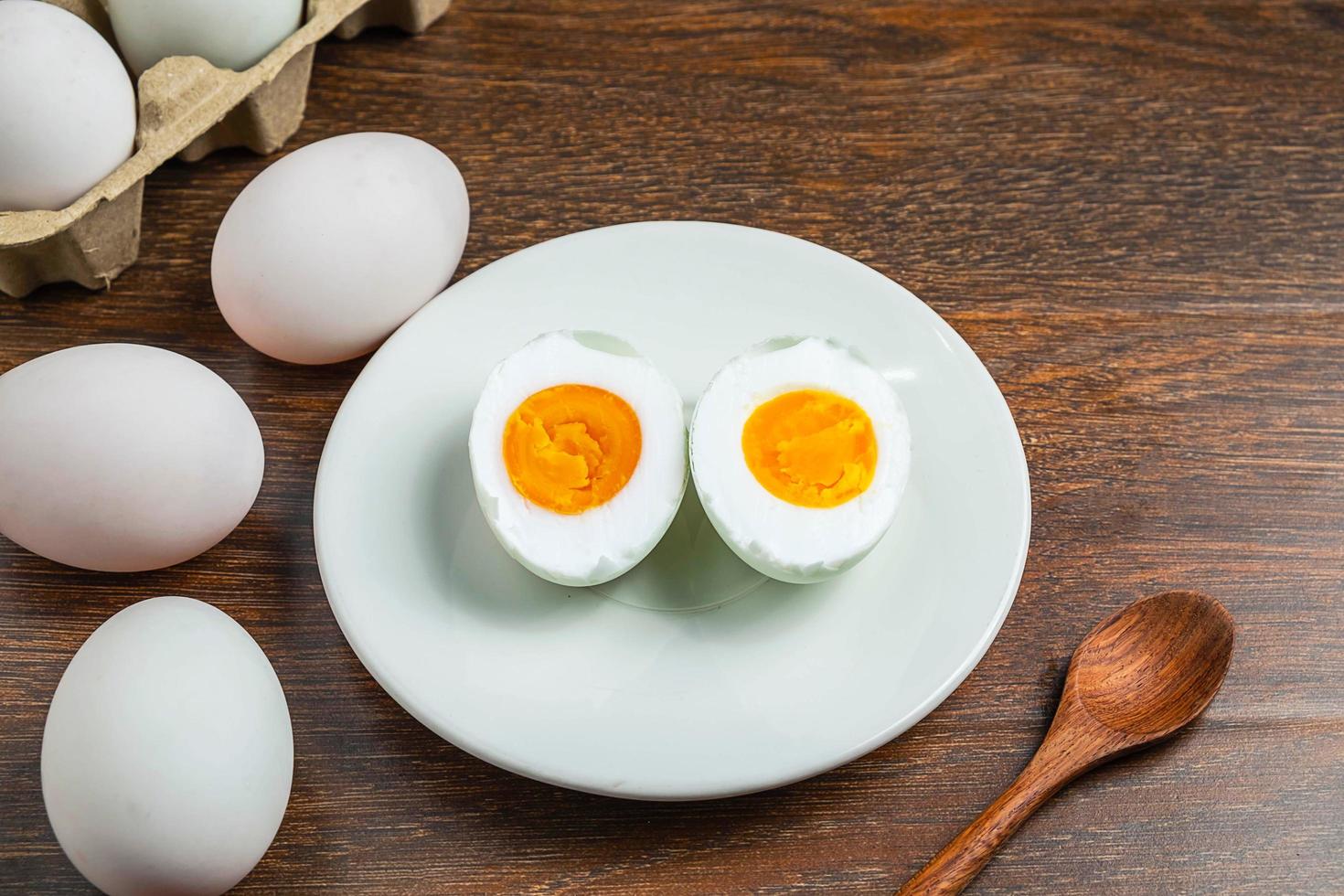 Sliced hard-boiled duck egg on a white plate next to whole eggs in a carton on a wooden table photo