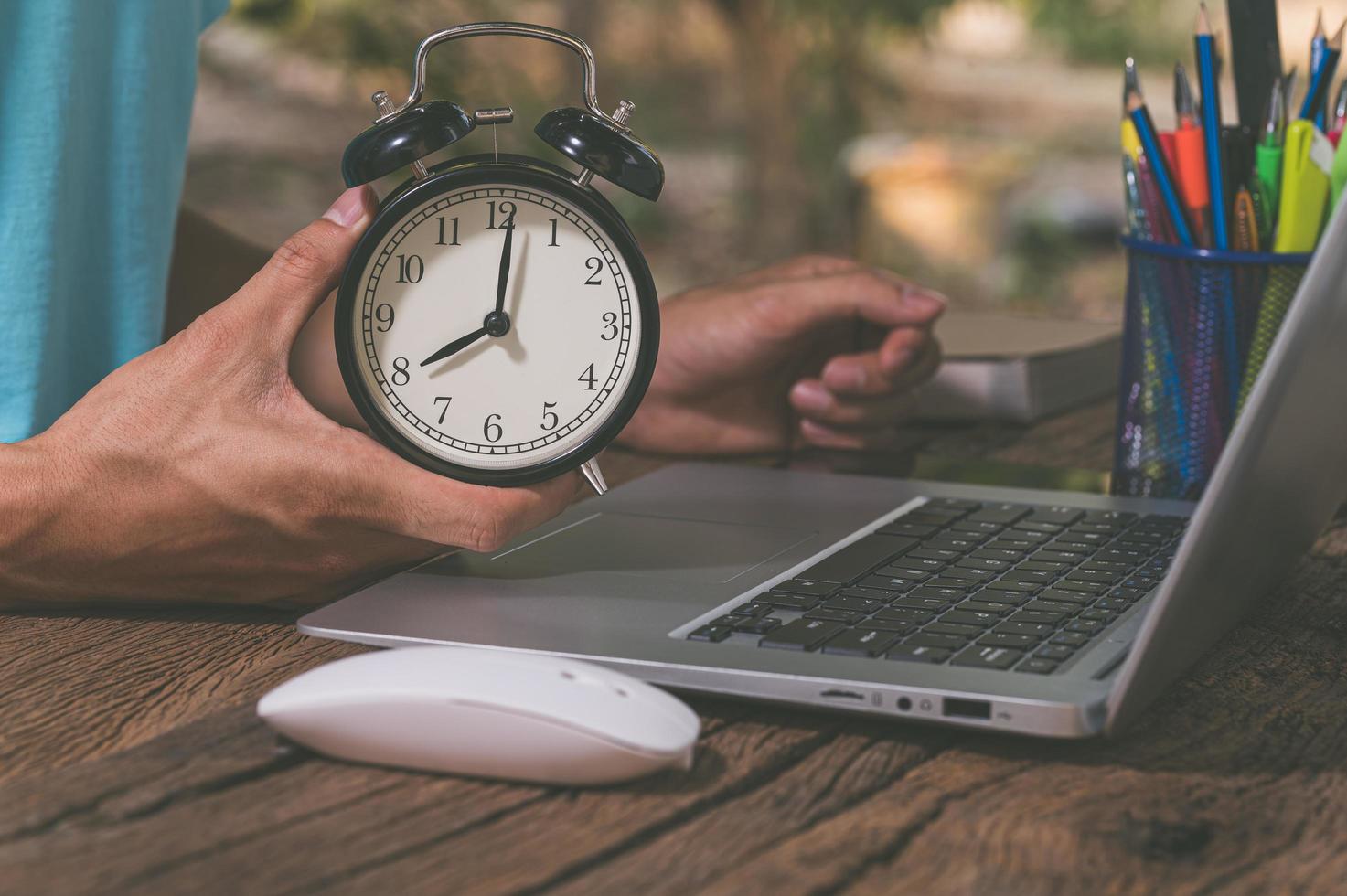 Hand holding a clock at the work desk photo