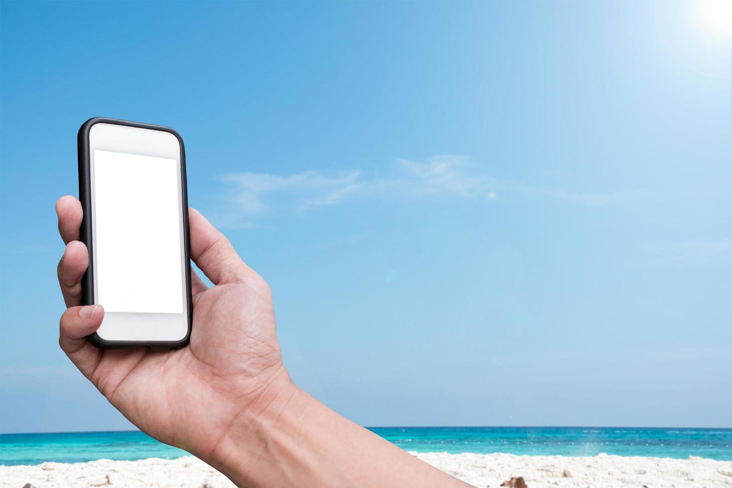 Hand holding a smartphone over a beach and a blue sky background photo