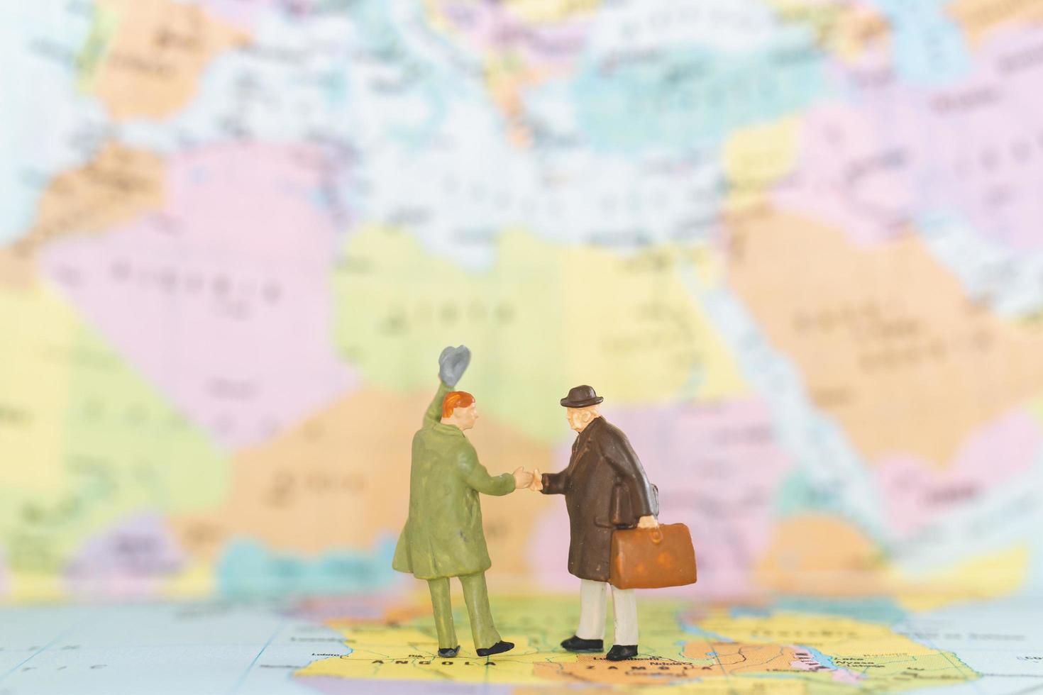 Miniature tourists handshaking on a world map background, journey and travel concept photo