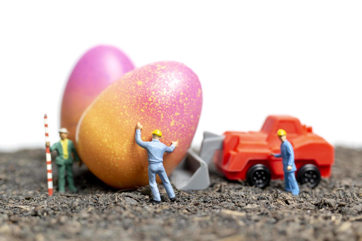 Miniature people working on Easter Eggs for Easter day with a white background photo