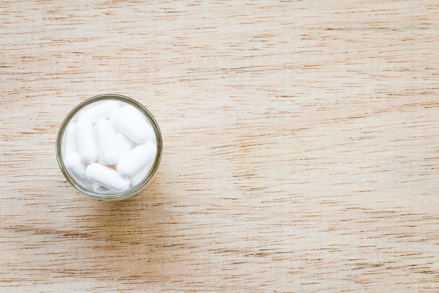 White pills in a glass on a wooden background photo