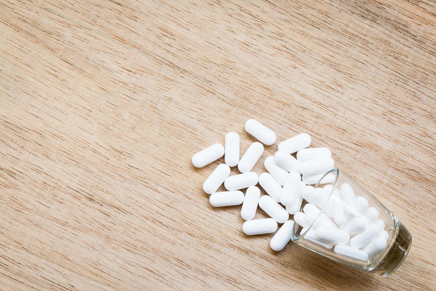 Pastillas blancas en un vaso sobre un fondo de madera foto