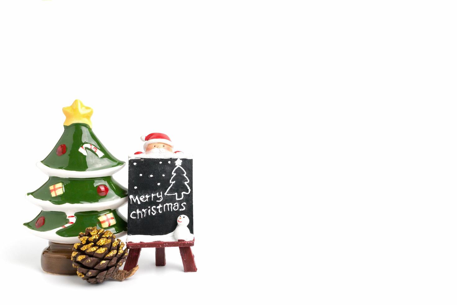 Figurilla de Papá Noel con una pizarra en miniatura con texto feliz Navidad sobre un fondo blanco. foto
