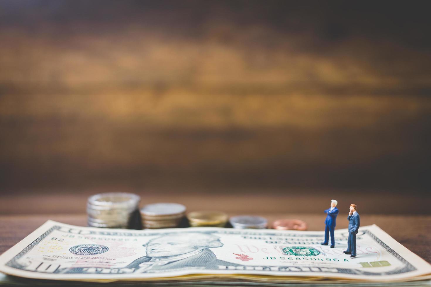 Miniature businessmen on money on a wooden background photo