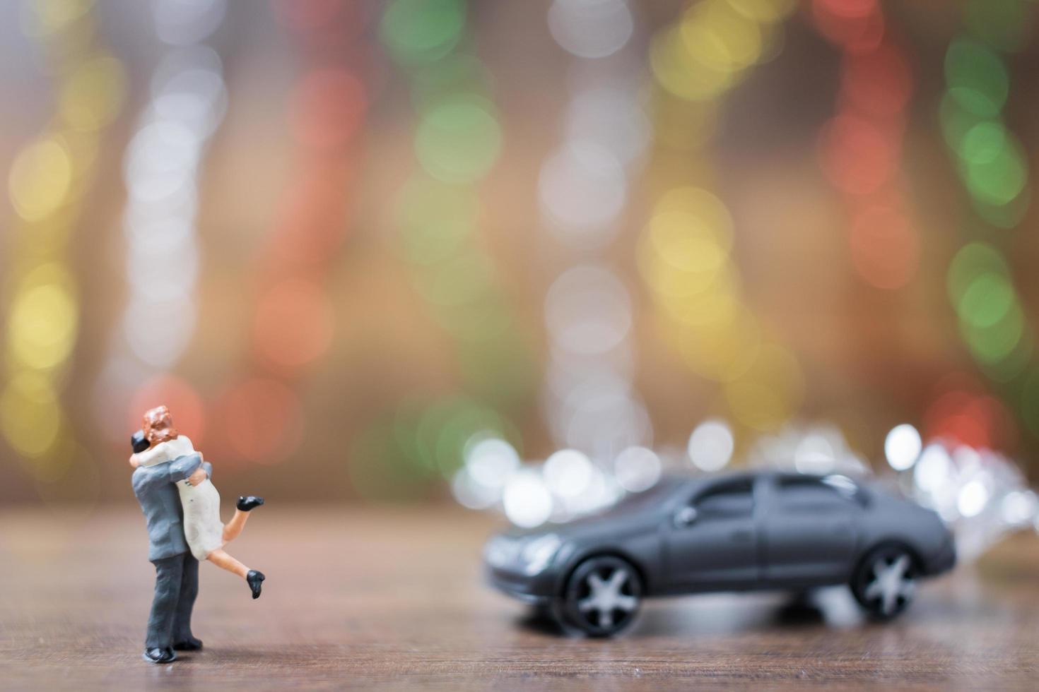 Pareja en miniatura abrazándose en un piso de madera con un colorido fondo bokeh, concepto de familia exitosa foto