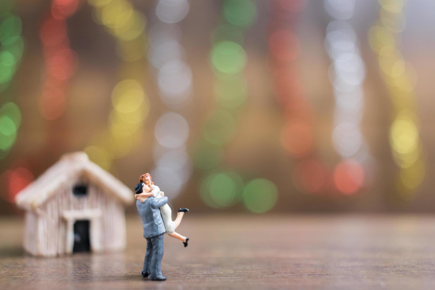 Pareja en miniatura abrazándose en un piso de madera con un colorido fondo bokeh, concepto de familia exitosa foto