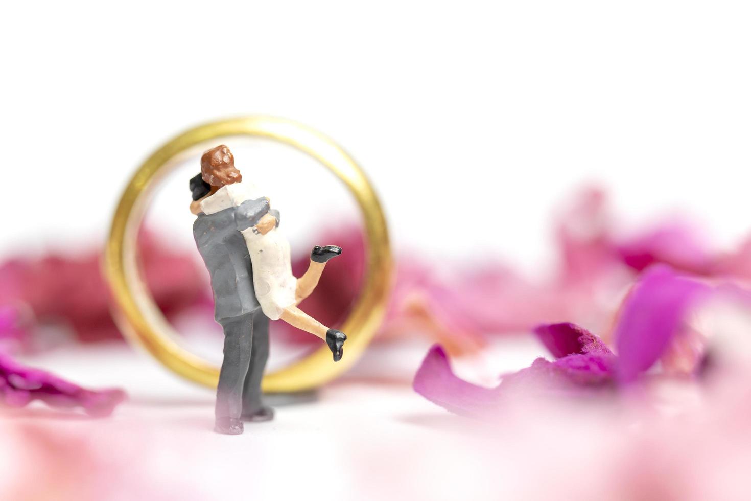 Miniature couple hugging with a wedding ring and pink petals isolated on a white background photo