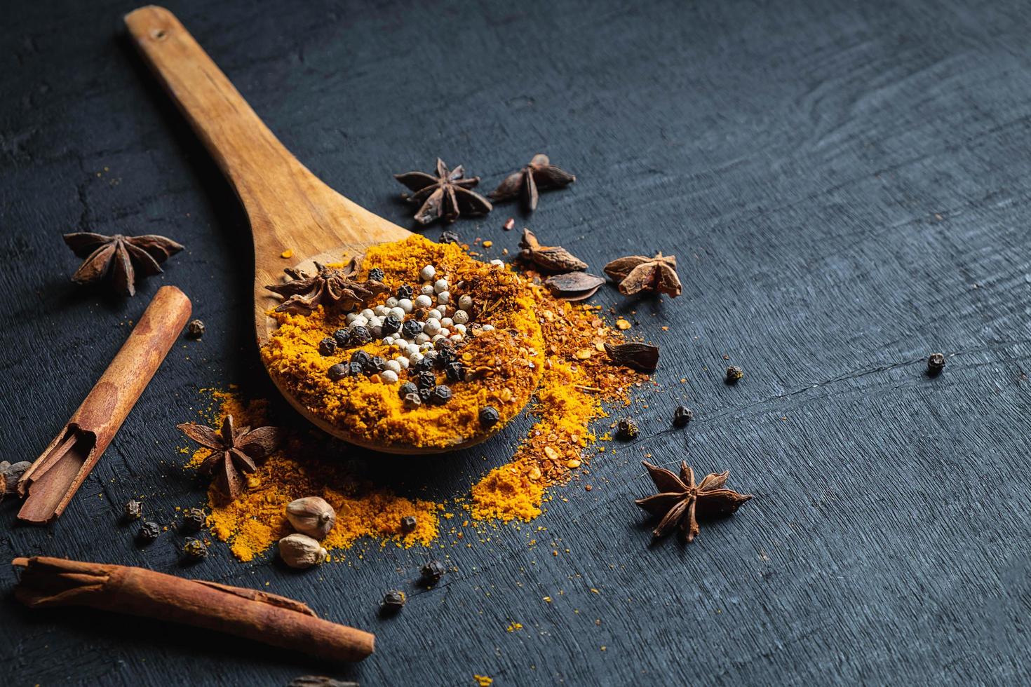 Colorful spices and powder on a wooden spoon on a black table background photo