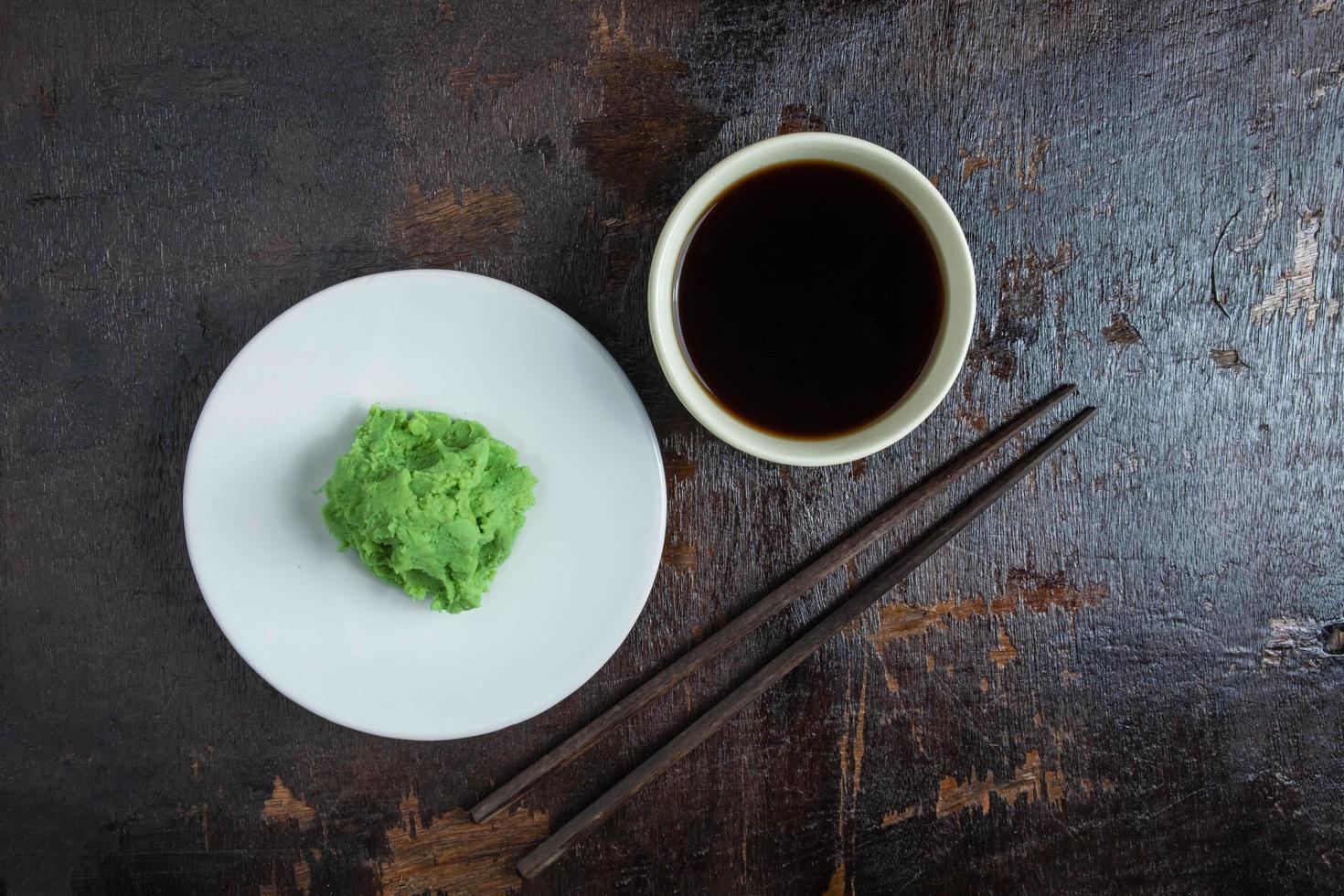 salsa de soja en una taza blanca y wasabi en una placa blanca sobre un fondo de madera negra foto