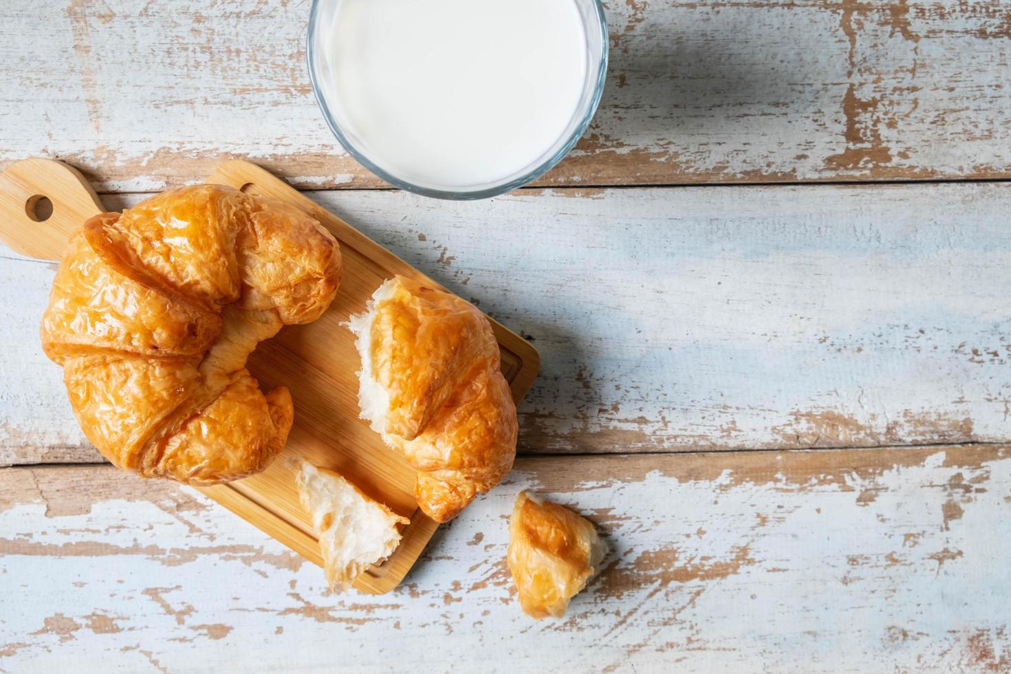 Croissants sobre una tabla para cortar madera junto al vaso de leche en la mesa de madera azul foto