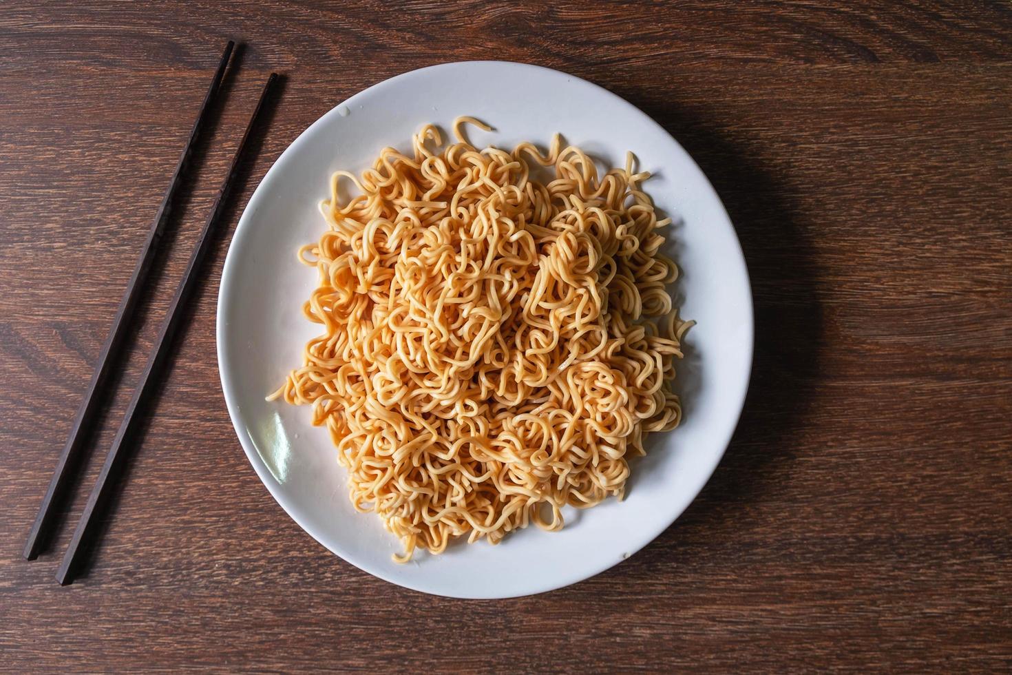 Instant noodles on a white plate next to pair of chopsticks on a wooden table photo